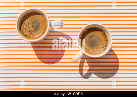 Two white coffee cup on orange striped table at direct sunlight. Top view with shadow Stock Photo
