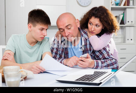 Parents with teenager son using laptop and analyzing their finances with documents at table Stock Photo