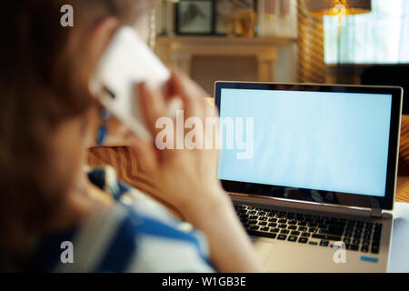 Over shoulder shot of young housewife laying on couch at modern home in sunnny hot summer day calling robot customer support while looking at laptop b Stock Photo