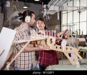 Team of aircraft enthusiasts working in workshop on creating of airplane models, checking design in drawings Stock Photo