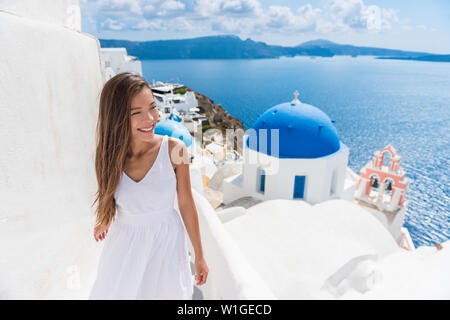 Santorini travel tourist woman on vacation in Oia walking on stairs. Person in white dress visiting the famous white village with the mediterranean sea and blue domes. Europe summer destination. Stock Photo