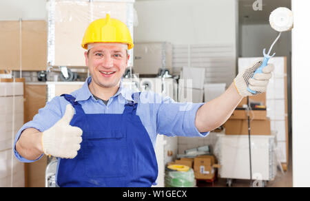 Happy professional construction worker painting wall in repairable room, giving thumbs up Stock Photo