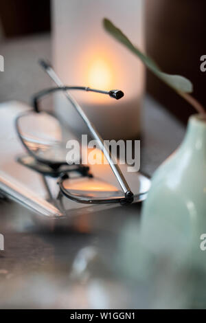 eye glasses folded up on a tables reflecting  the light of a candle Stock Photo