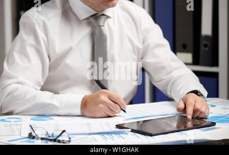 Businessman working with tablet pc, calculating, reading and writing reports. Office employee, table closeup. Business financial accounting concept. Stock Photo