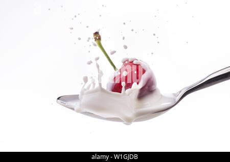 a cherry falls into a spoon full of yogurt creating a splash Stock Photo