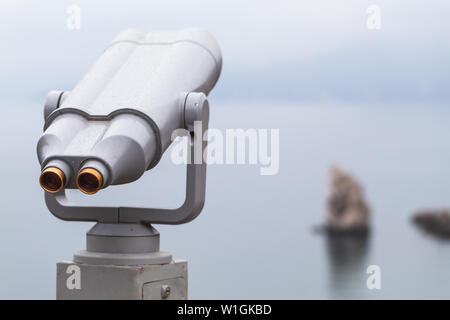 Binocular telescope on a rotating base mounted on an outdoor touristic viewpoint. Close up photo with blurred seascape on a background Stock Photo