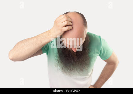 Portrait of middle aged bald man with long beard in light green t-shirt standing and showing his baldness on his head. indoor studio shot, isolated on Stock Photo