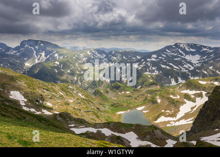 Amazing green and yellow colors of sunlit Rila mountain landscape with impressive distant peaks covered by snow, beautiful lakes and dramatic sky Stock Photo