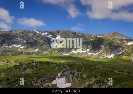 Amazing light on a green, grass covered highlands of Rila mountain, epic, pointy, rocky peaks and blue sky on a tour of seven Rila lakes Stock Photo