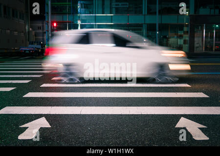 white car quickly drives through the pedestrian zebra. Pedestrian crossing with directional arrows at night. pedestrian marking on wet pavement. red s Stock Photo