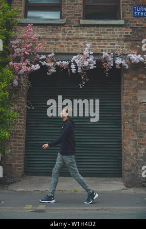 Man in his early 30's walking on the streets of Manchester past a colourful graffiti wall. Stock Photo