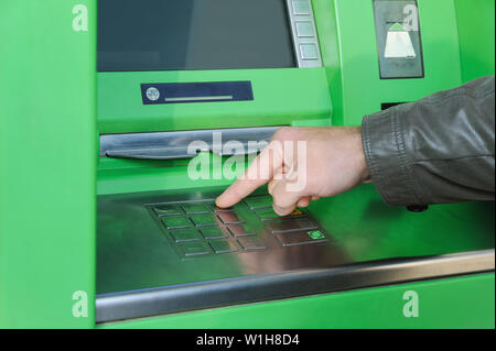 A man's hand is pushing the buttons to enter the pin code in the ATM. Stock Photo