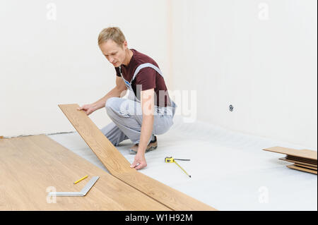 Installation of a laminate floorboard. The worker is attaching one bar after another. Stock Photo
