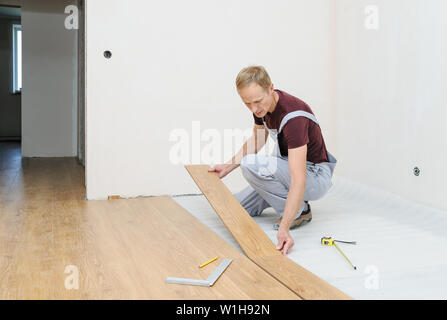 Installation of a laminate floorboard. The worker is attaching one bar after another. Stock Photo