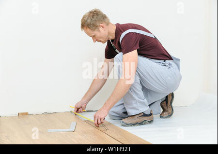 Installation of a laminate floorboard. The worker is measuring the distance to the wall. Stock Photo