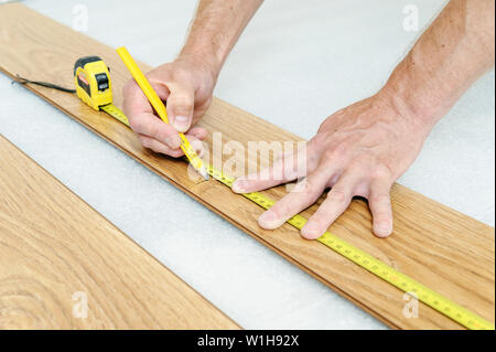 Installation of a laminate floorboard. Worker's hands are measuring a piece of board to cut into the future. Stock Photo