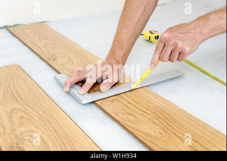 Installation of a laminate floorboard. Worker's hands are marking the cutting line. Stock Photo
