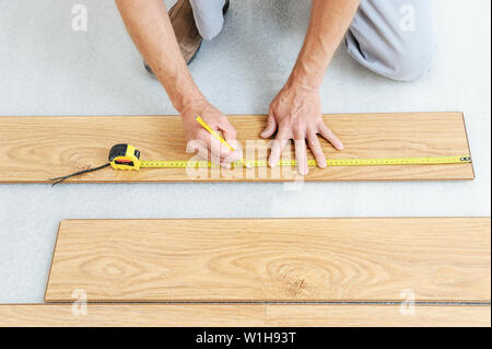 Installation of a laminate floorboard. Worker's hands are measuring a piece of board to cut into the future. Stock Photo