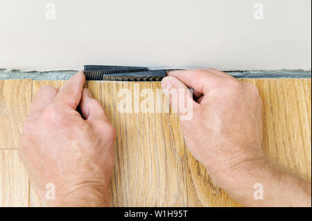 The worker's hands are placing a wedges between the wall and the floorboard. Stock Photo