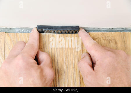 The worker's hands are placing wedges between the wall and the floorboard. Stock Photo