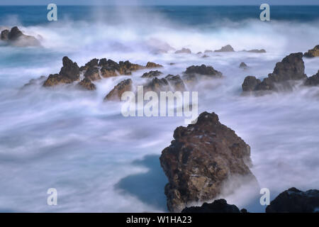 Excerpt from the Atlantic Ocean on teneriffa with waves and spray over black lava stones. Long exposure photography with ND filter, the water is misty Stock Photo