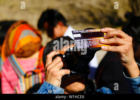 La Paz, Bolivia 2nd July 2019: A man takes a photo of a partial eclipse of the sun while holding a solar eclipse filter over the end of the camera lens at an eclipse watching event near the city centre. In La Paz the eclipse lasted for about 2 hours 10 minutes with about 55% coverage at its maximum. Stock Photo