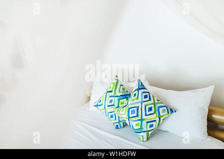 Two colorful blue and green ornamental pillows on white bed. Light cozy interior design. Empty place. Stock Photo