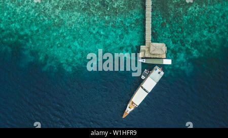 Aerial view of pier with yacht on tropical island with coral reef coastline. Cruise and luxury boat travel concept. Directly from above. Stock Photo