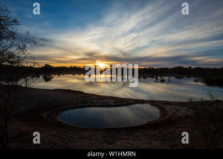 Dramatic sky, trees in silhouette and reflections on water at dusk in the Australian Outback Stock Photo