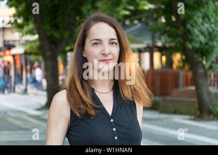 Portrait of a mature woman, 40s, looking camera with soft smile, outdoors in a city. Stock Photo