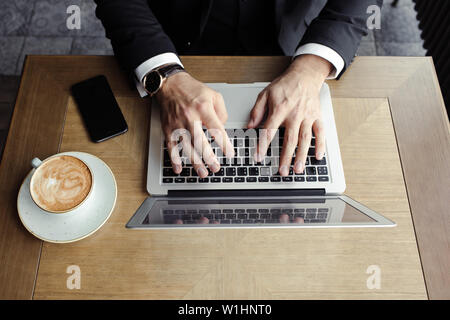 hands men lie on the laptop, near a phone and cappuccino Stock Photo