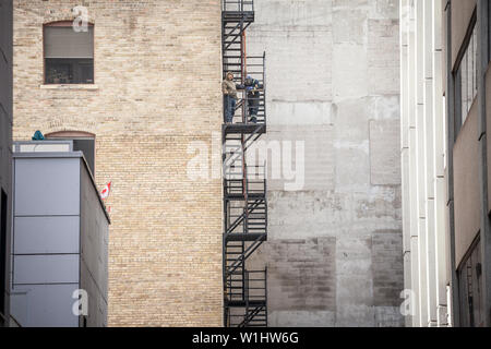 TORONTO, CANADA - NOVEMBER 14, 2018: Construction workers fixing Fire escape rusty stairs and ladders, in metal, on a typical North American old brick Stock Photo