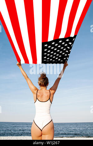 Beautiful patriotic woman holding an American flag on the beach.  USA Independence day, 4th July. Freedom concept, view from the back.