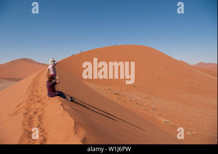 Hikers climbing up a sand dune ridge at Sossusvlei, Namib-Naukluft National Park, Namibia. Stock Photo