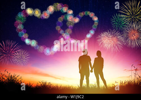 young couple watching heart shape fireworks on hill Stock Photo