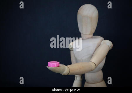 sinlgle close up figure holding a small pink pill. cold and flue or party drug recreational illicit drug testing concept. Personal choice strength cha Stock Photo