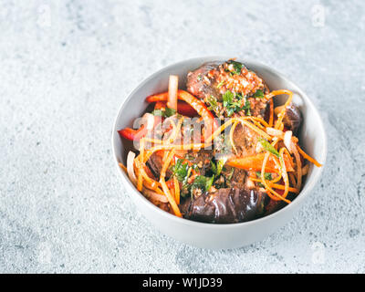 Salad of pickled eggplant, carrot, onion, sweet pepper in bowl on gray cement background. Fermented food. Preserved vegetables. Copy space for text. Stock Photo