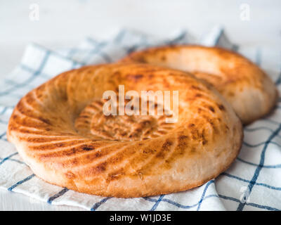 Tasty fresh tandoor bread on white wooden table. Two tandoor flat bread cake on linen kitchen towel or napkin. National asian meal, food, bread. Stock Photo