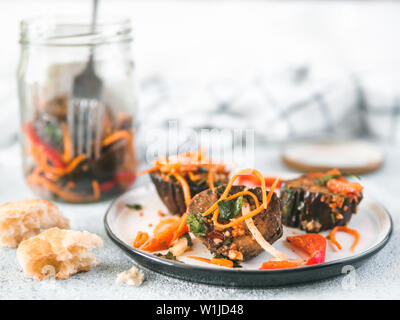 Salad of pickled eggplant, carrot, onion, sweet pepper on plate over gray cement background. Preserved vegetables in glass jar on background. Fermented food. Copy space for text. Stock Photo