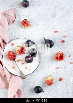Half and whole figs on gray cement or stone background. Ripe violet figs with copy space for text. Figs flesh in teaspoon on plate and figs on tabletop. Top view or flat lay. Vertical. Stock Photo