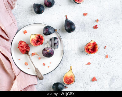 Half and whole figs on gray cement or stone background. Figs flesh in teaspoon on plate and figs on tabletop. Top view or flat lay. Horizontal Stock Photo