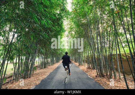 Young man lift wheeling with vintage bike in bamboo forest Stock Photo