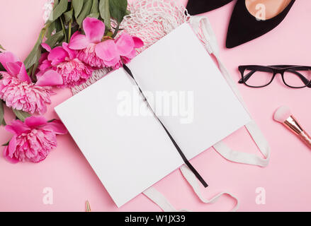 Open notepad mock-up on the table with feminine accessories and pink peonies, top view Stock Photo