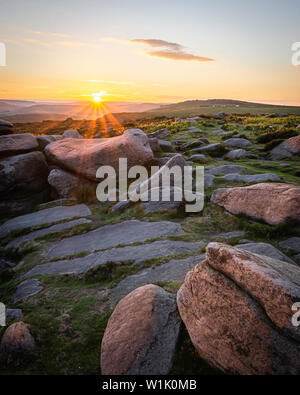 Sunset scene in rural Peak District, Derbyshire, UK.Stones on top of the hill lit by sun setting behind horizon.Ethereal evening scenery.Landscape ima Stock Photo