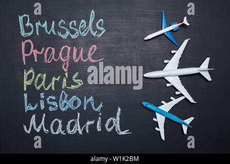 Traveling concept. Toy plane over chalkboard with cities written on it Stock Photo