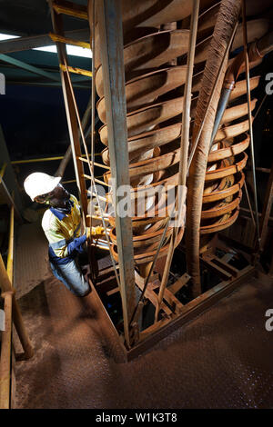 Mining operations for transporting and managing iron ore. Interior of saprolite test plant at dawn & operator adjusting spiral on cyclone concentrator Stock Photo