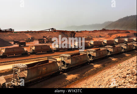 Rail head train operations on iron ore mine. Loaded ore train on rail loop waiting to leave for port. Stock piling behind with train being loaded.