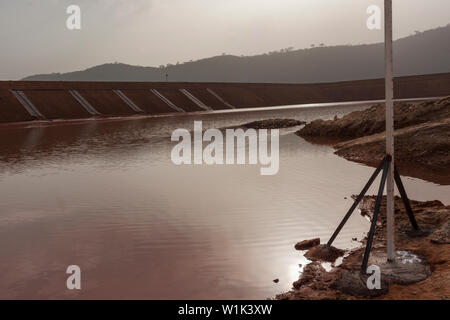 Mining operations for transporting and managing iron ore. Construction of dam wall for tailings storage facility and water effects into sun. Stock Photo