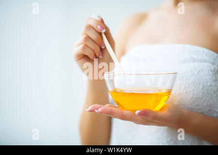 Female hand and orange paraffin wax in bowl. Stock Photo