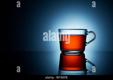 Tea in a transparent tea cup on moody reflective surface and blue background with copy space. Advertisement product shoot. Stock Photo